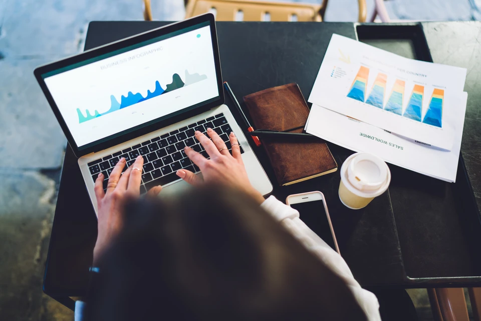 Personne travaillant sur ordinateur portable dans un environnement professionnel, consultant des graphiques et données analytiques à l'écran
